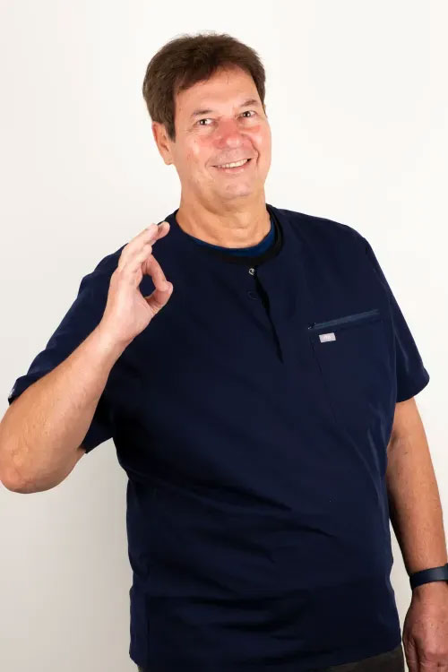 The image features a man standing with his right hand raised to his face, making an  OK  gesture, against a plain background. He is wearing a dark blue t-shirt and has short hair.