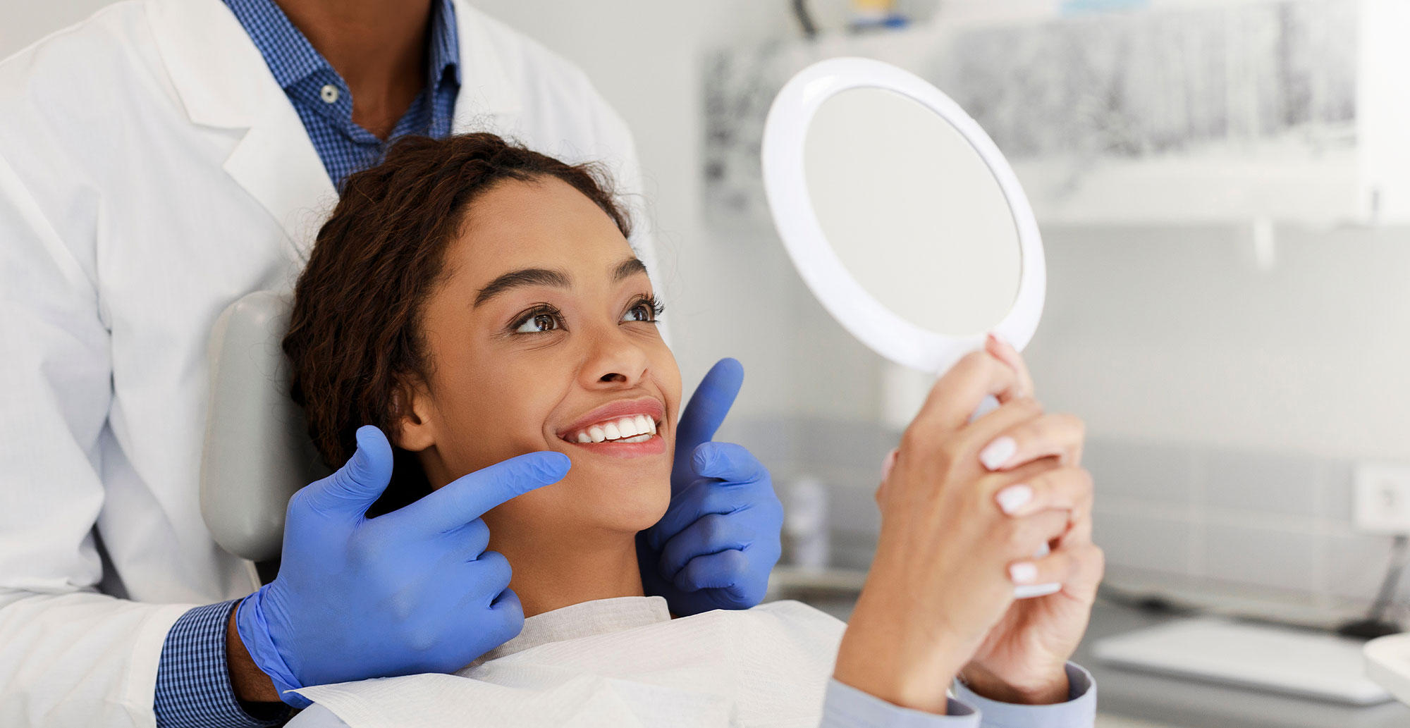 A dental professional is assisting a patient with a magnifying glass, likely during an examination or treatment.