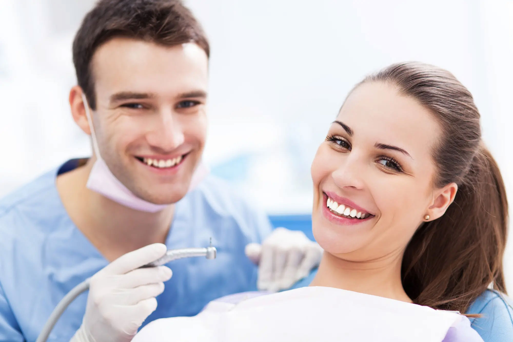 A man and woman in medical attire, with the man holding a dental drill, smiling at the camera.