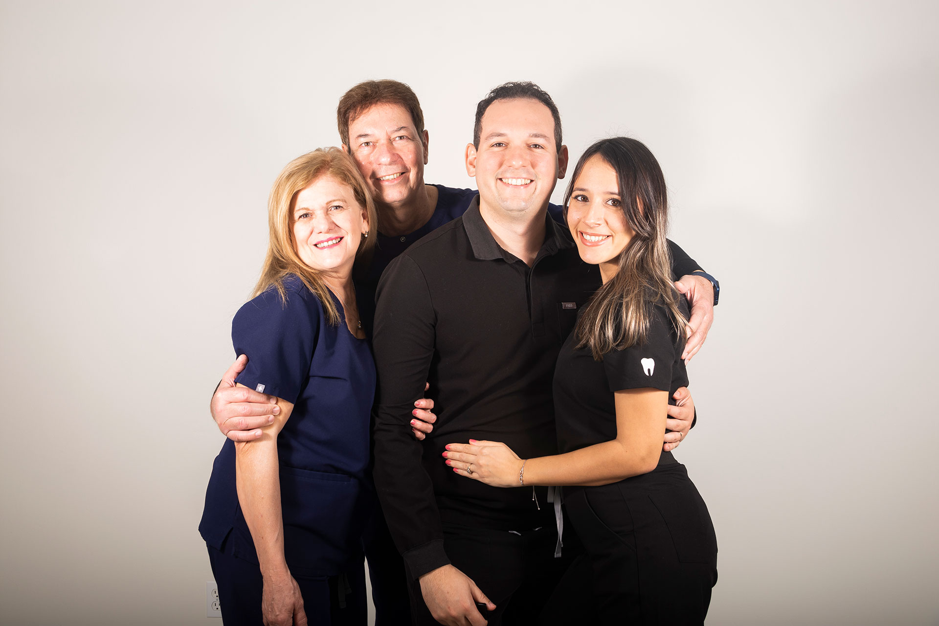 The image shows a group of four people posing together for a photograph, with two individuals embracing and the other two standing behind them.