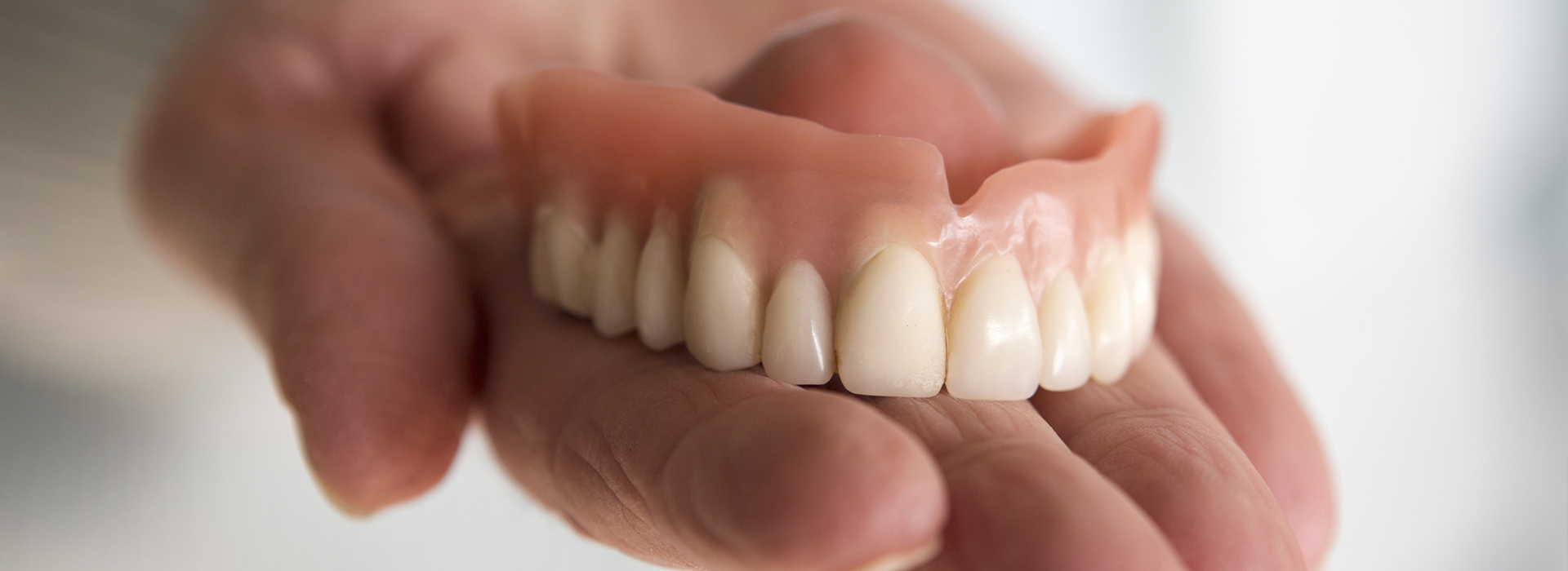 A person s hand holding a set of dentures, showcasing the upper and lower teeth with visible ridges.