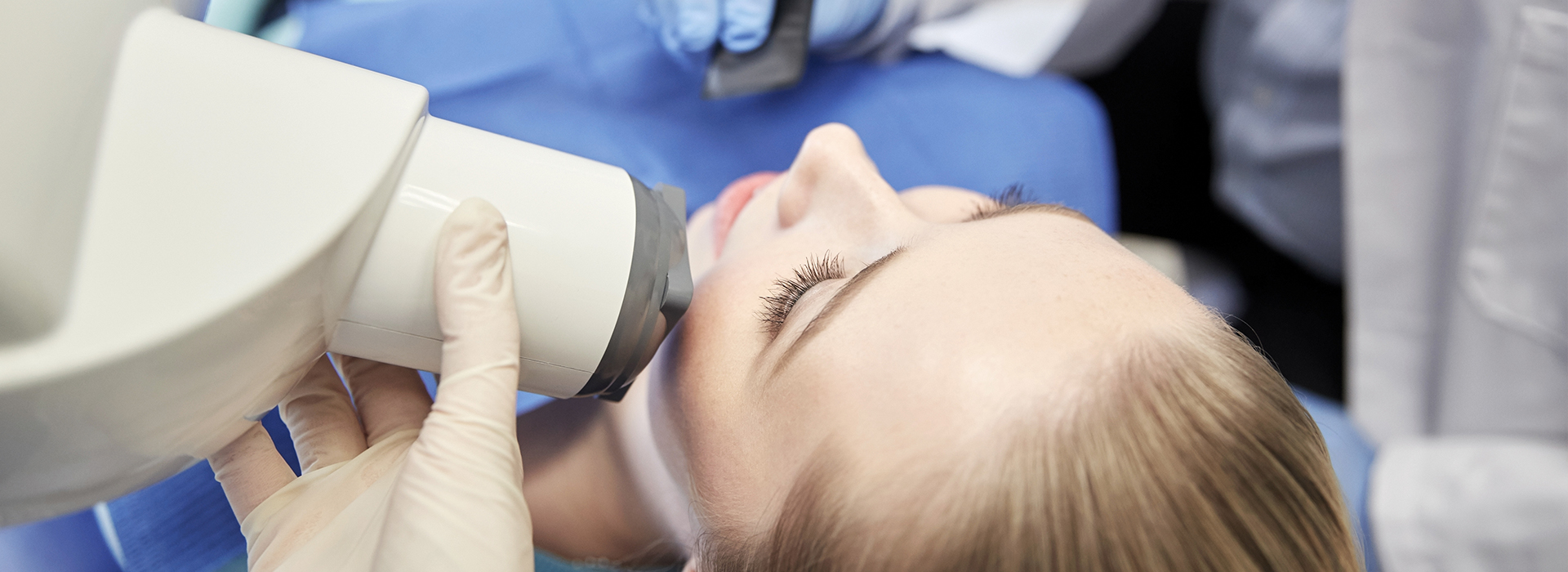 A woman receiving a dental procedure with a dentist using a microscope to examine her teeth.