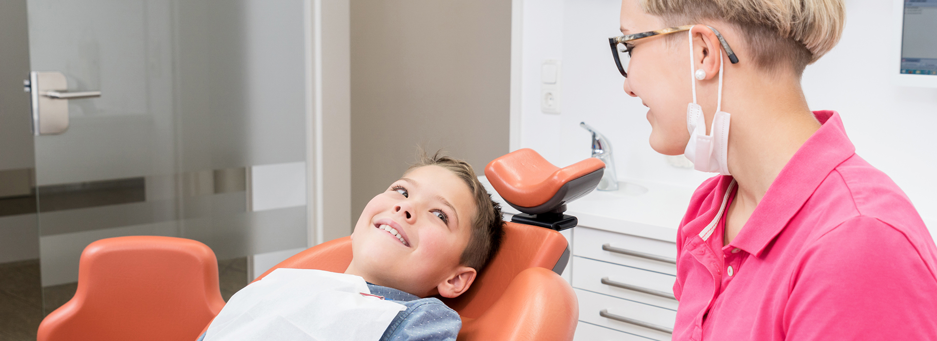 An image of a dental office, featuring a dentist and a patient in the chair.