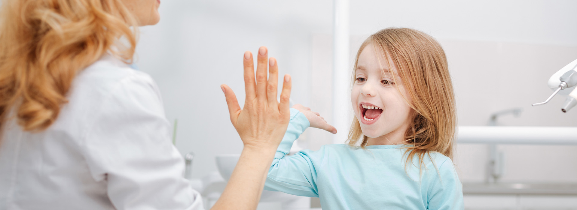 A mother and daughter in a dental office, with the mother assisting the child during a dental checkup.